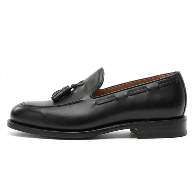 Side profile view of a black leather tassel loafer for men, featuring a handcrafted apron toe, sleek stacked heel, and premium leather sole on a minimalist white background.