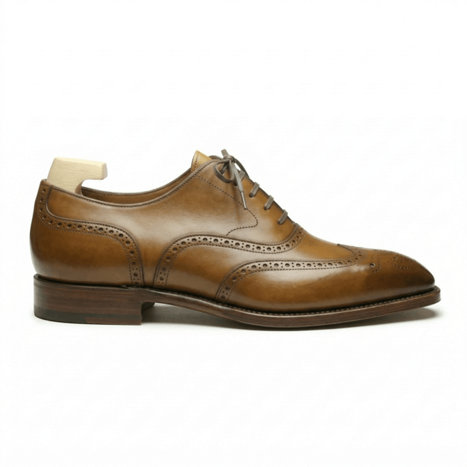 Side view of a premium tan leather wingtip brogue shoe for men with handcrafted medallion toe detailing and a classic lace-up oxford silhouette.