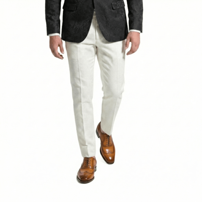 Front view of a man wearing a black floral jacquard blazer, off-white tailored linen trousers, and tan leather wingtip brogue dress shoes.