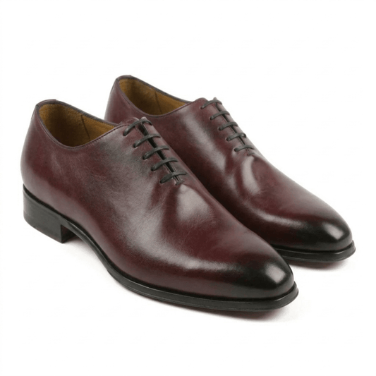 A pair of luxurious handcrafted burgundy wholecut Oxford shoes made from premium full-grain leather with a burnished finish and sleek black laces on a white background.