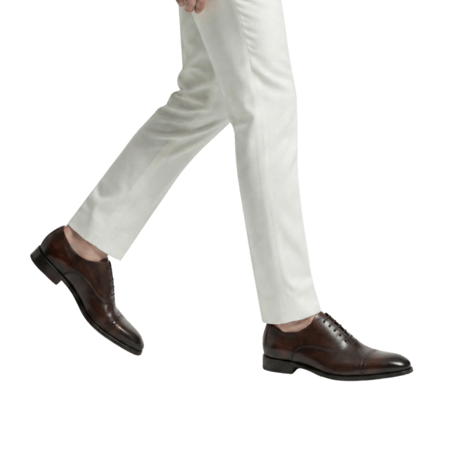 Dark brown leather oxford shoes paired with white trousers front walk