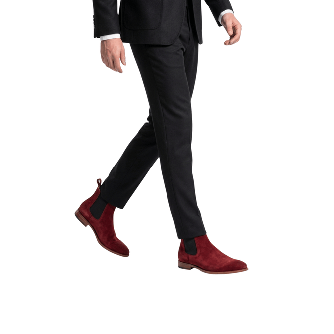 Side profile action shot of a man wearing luxury burgundy suede boots with leather soles and black elastic side panels.