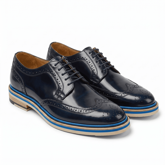 A pair of navy blue leather wingtip brogues featuring traditional decorative perforations and a modern multi-layered blue and tan sole.