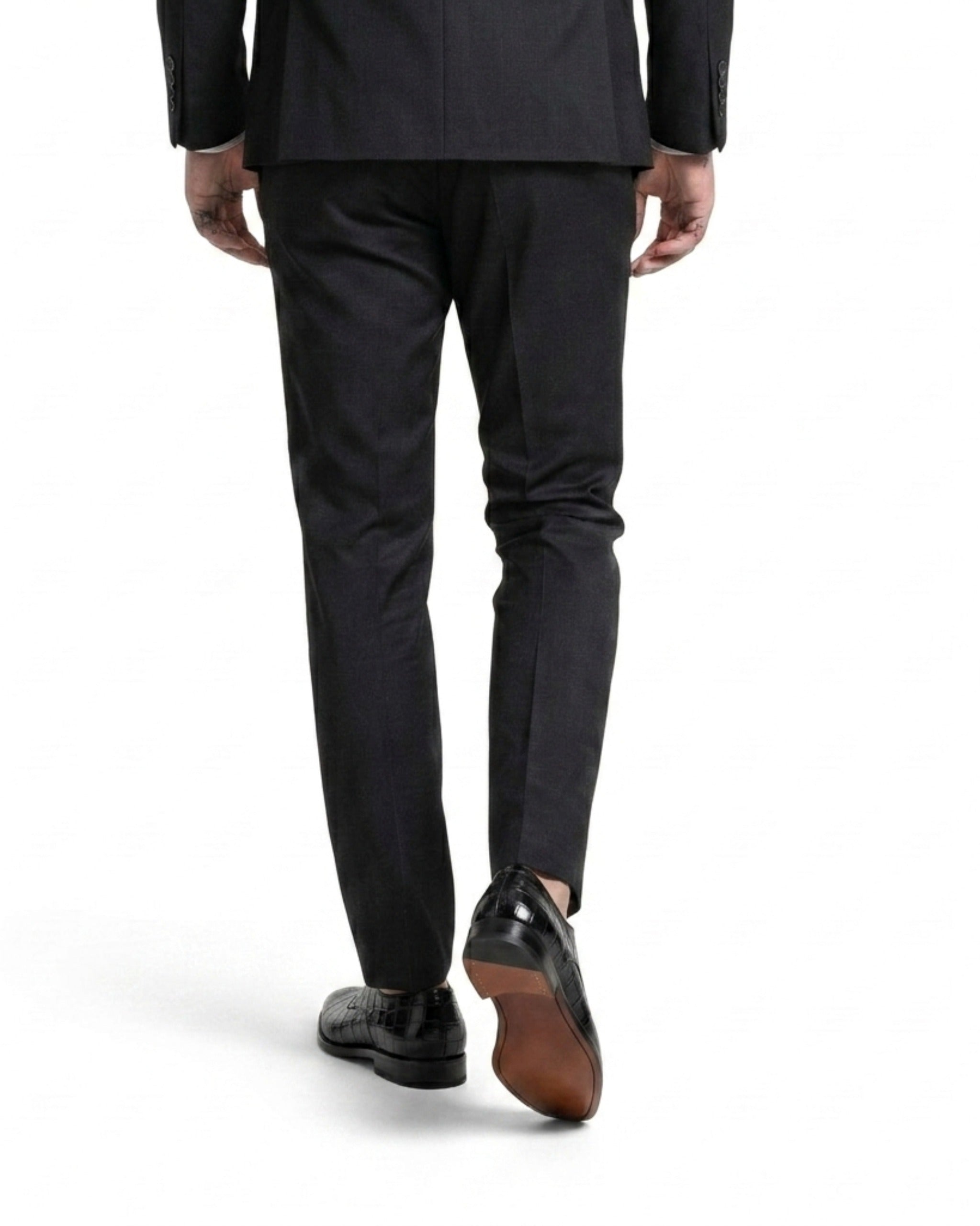 Rear view of a man walking in black crocodile-textured shoes, highlighting the stacked heel and natural leather sole.