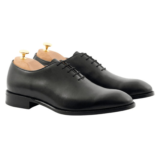 A pair of luxurious black leather wholecut Oxford shoes featuring a seamless handcrafted design, displayed with premium wooden shoe trees on a white background.