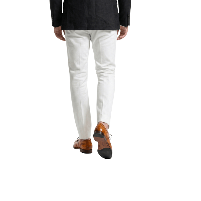 Rear view of a man walking in a black linen blazer, slim-fit white formal trousers, and handcrafted tan leather wingtip brogue shoes.