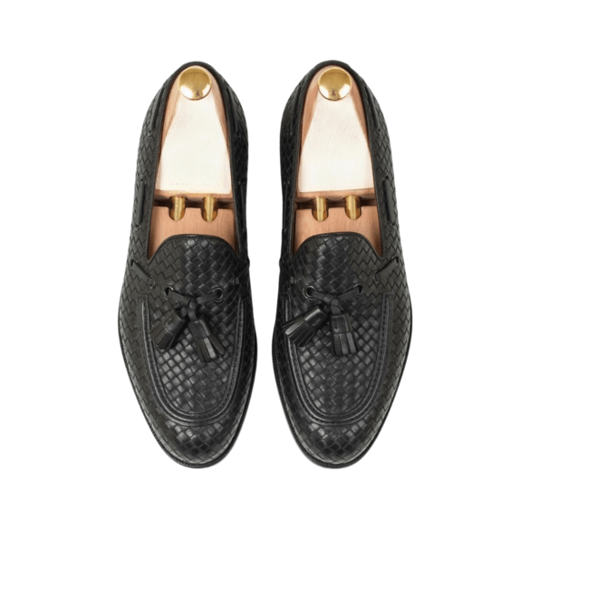 Flat lay of luxury black braided leather loafers featuring artisan tassel accents