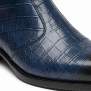 A detailed close-up showing the intricate texture of navy blue crocodile-embossed leather on a luxury men's boot with fine stitching and a polished finish.