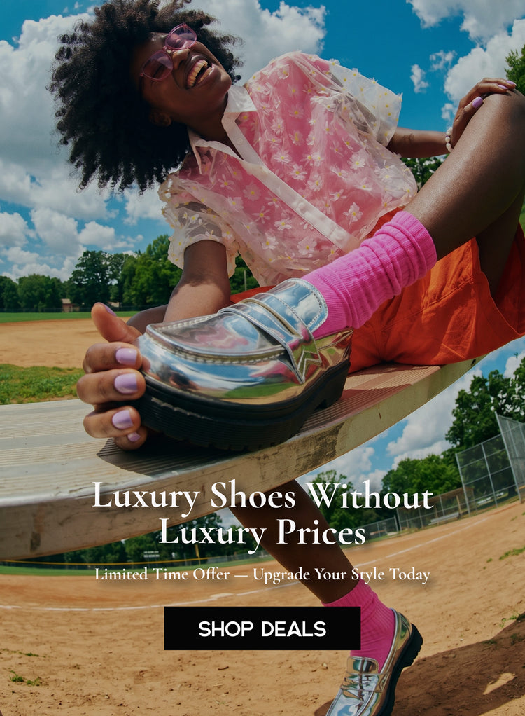 A woman wearing vibrant pink socks and metallic silver platform loafers on a sunny outdoor baseball field with a "Luxury Shoes Without Luxury Prices" promotional overlay.