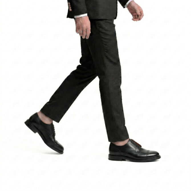 Side profile action shot of a man wearing premium black leather wingtip brogue oxfords, paired with tailored charcoal grey trousers and a formal suit jacket.