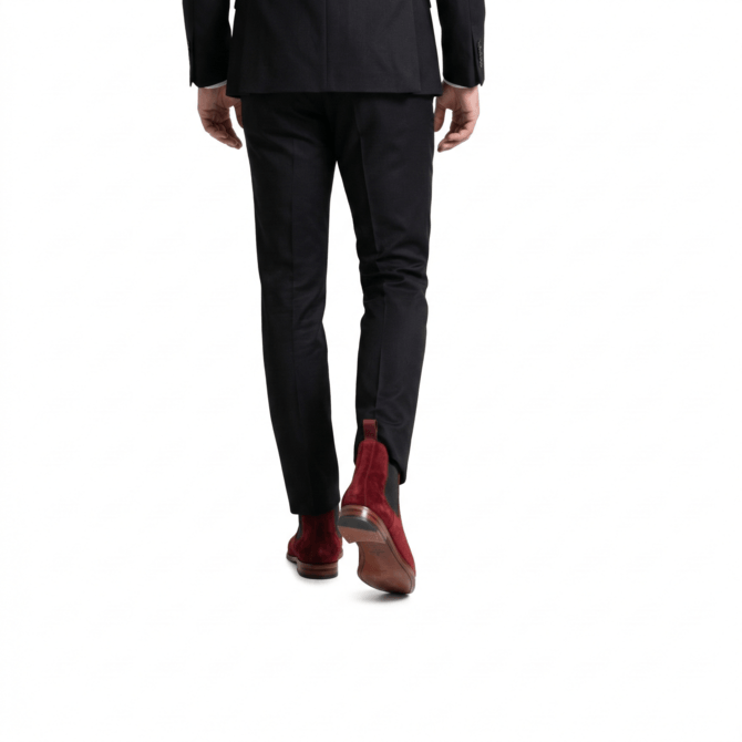 Rear lifestyle shot of men's burgundy suede boots with leather soles, styled with a black suit.