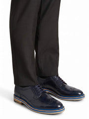 Professional lifestyle shot of the navy wingtip shoes styled with tailored black trousers.