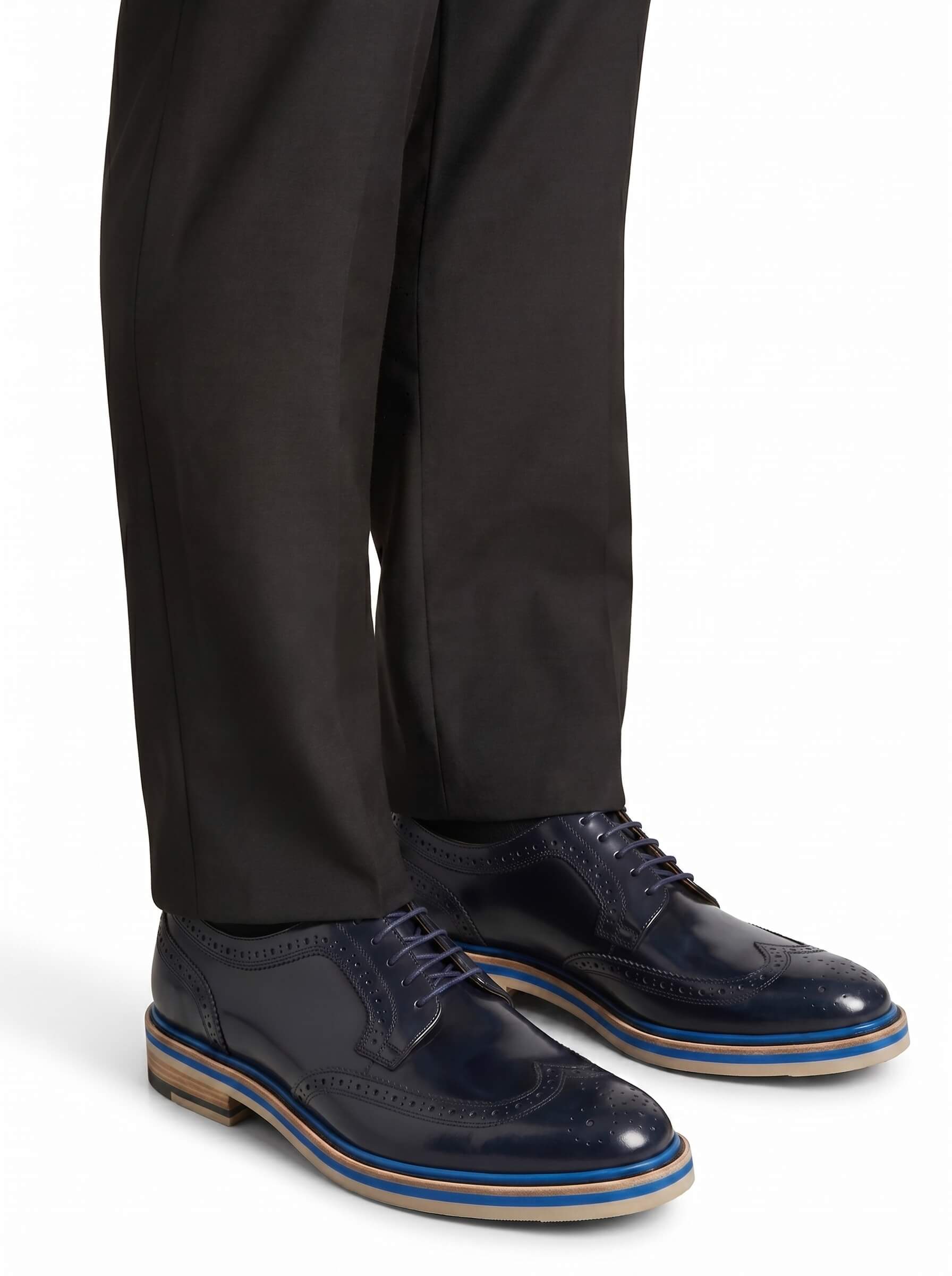 Professional lifestyle shot of the navy wingtip shoes styled with tailored black trousers.