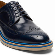 Macro close-up of the navy blue leather focusing on the intricate broguing and wingtip stitching.