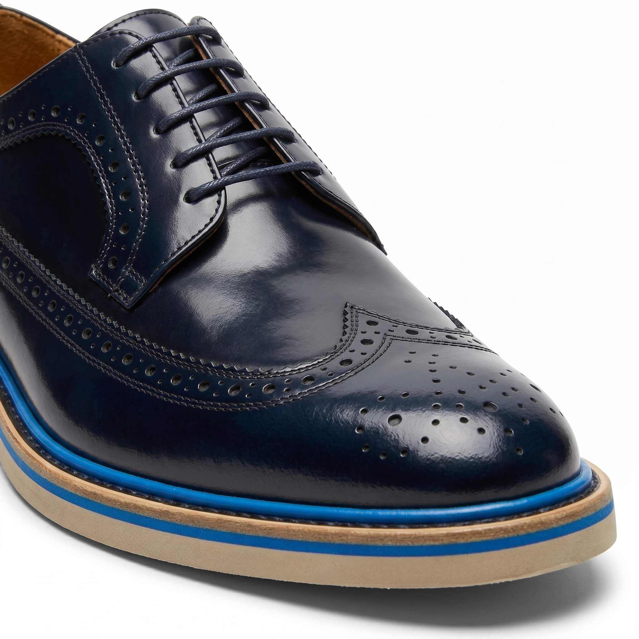 Macro close-up of the navy blue leather focusing on the intricate broguing and wingtip stitching.